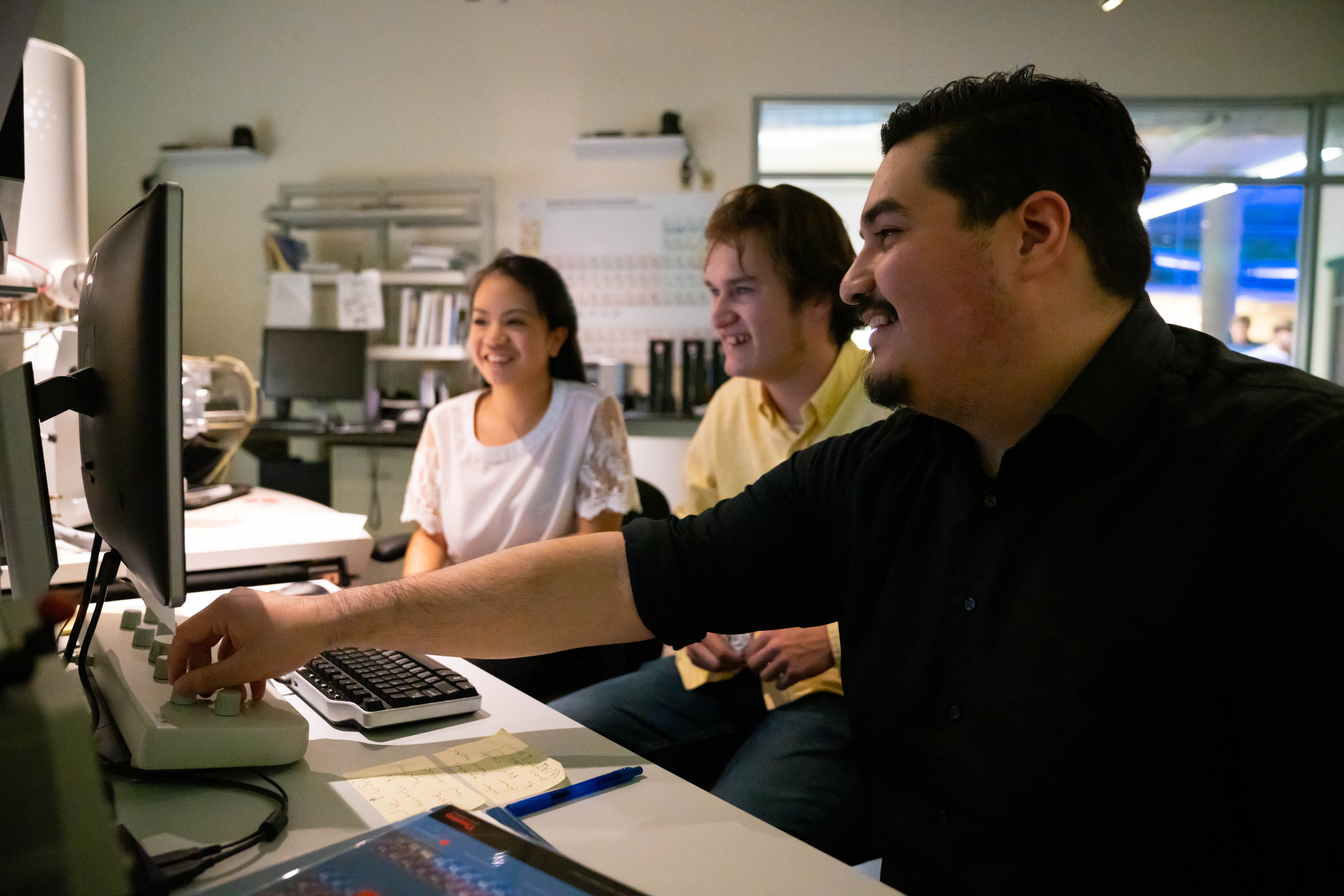 Three people are looking at a screen and smiling at a lab