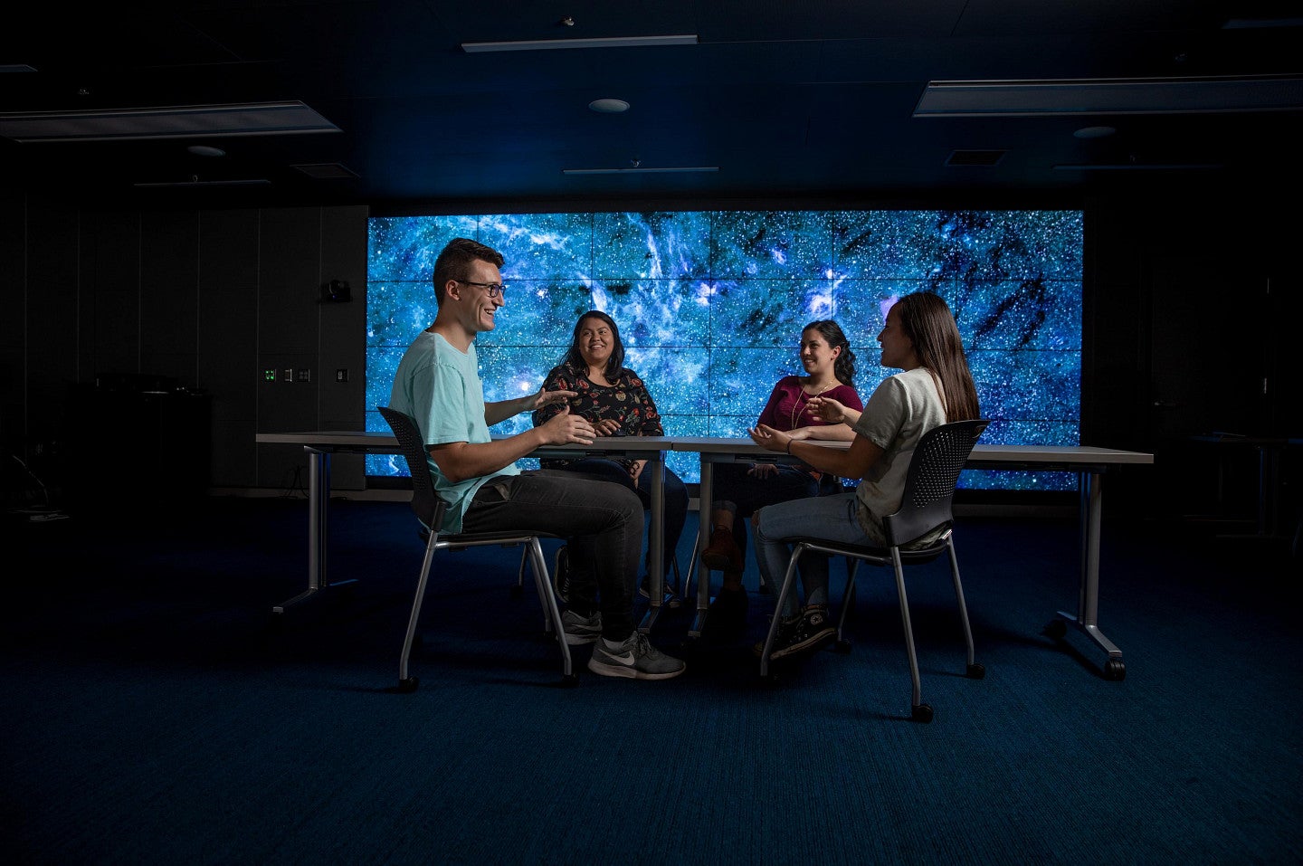 four students sit around table with colorful background