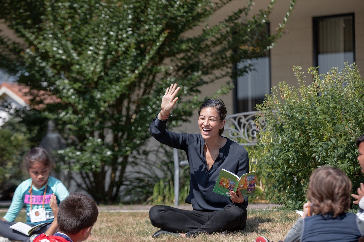 Woman seated cross legged on the grass reading to young children