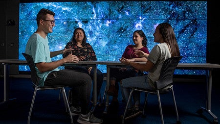four students sit around table with colorful background