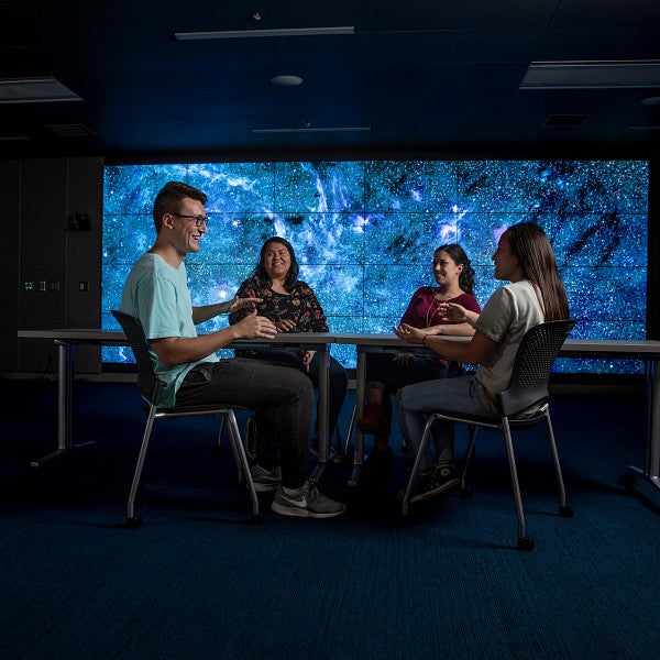 four students sit around table with colorful background