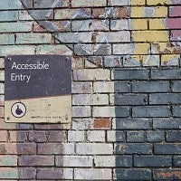 Brick wall covered in pastel chalk with sign that says "accessible entry" and has wheelchair icon
